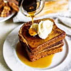 Square image of Slices of french toast stacked on a white plate with sliced bananas on top. maple syrup is being poured over the top of the French toast.