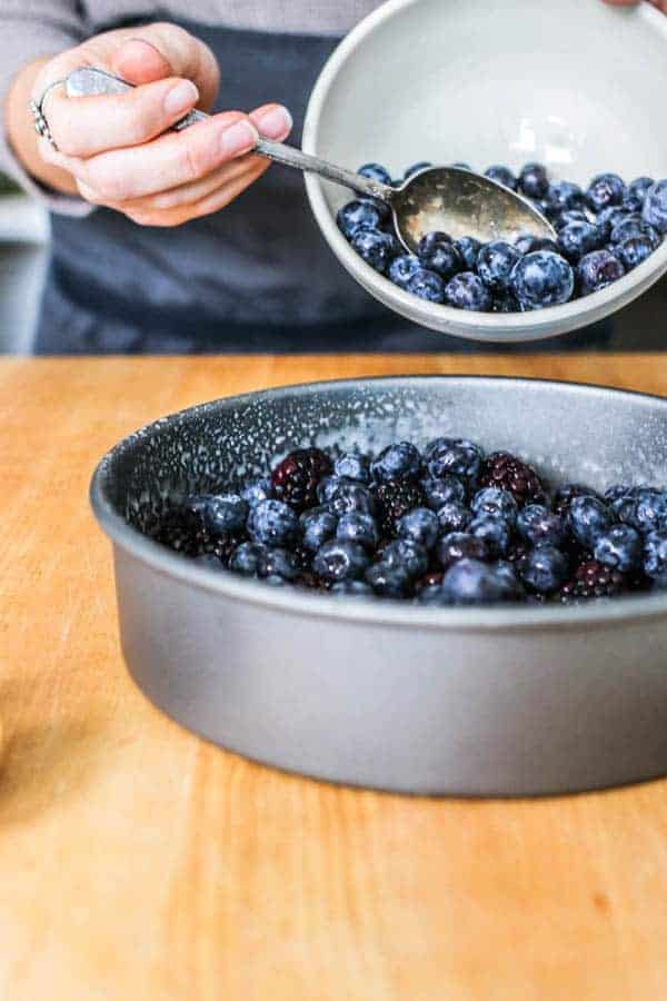 A bowl of blueberries being poured into a baking dish