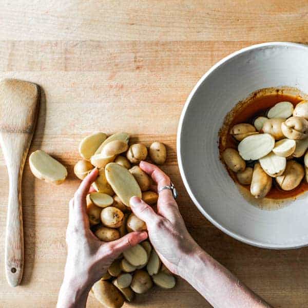 Picking up halved potatoes and placing into mixing bowls with spices