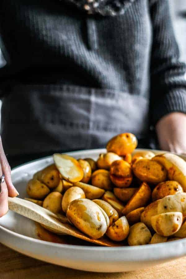 A woman stirring the spices and potatoes together to male crispy oven roasted potatoes