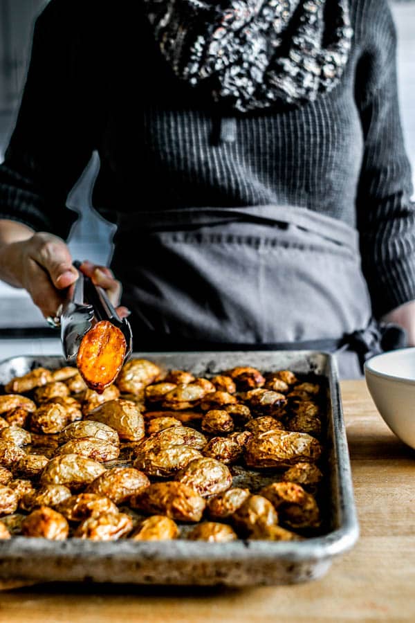 A woman holding up an oven roasted potato with tongs to show how crispy they are