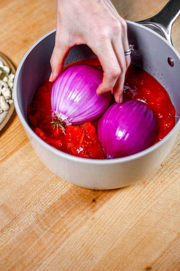 Onion halves being nestled into a saucepan with diced tomatoes