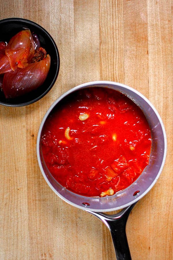 A sauce pan of cooked marinara sauce next to a bowl with cooked red onion