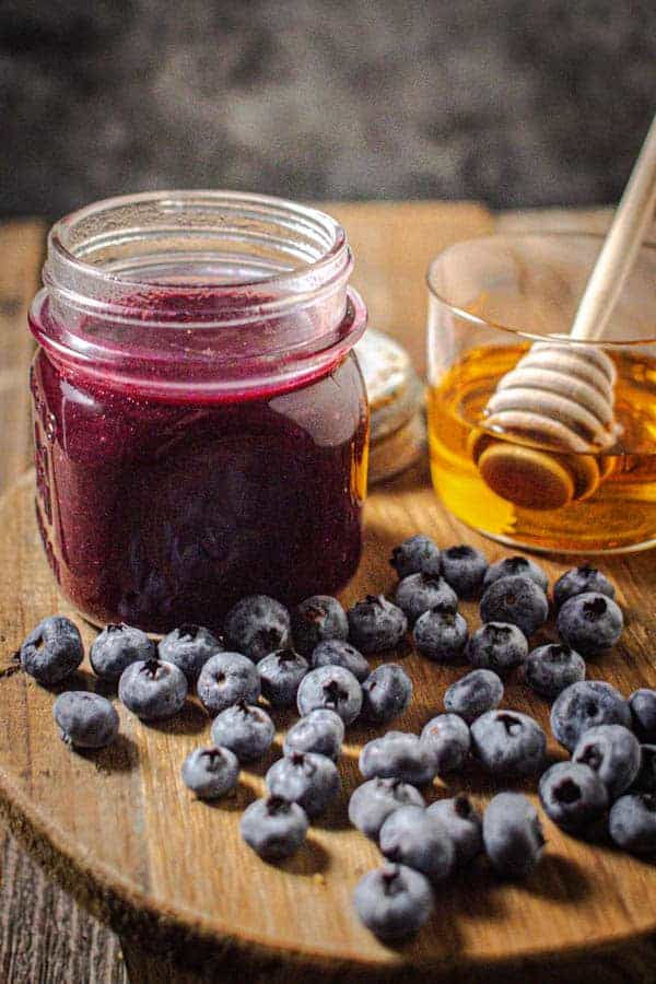 A jar of blueberry jalapeño sauce next to fresh blueberries and a jar of honey.