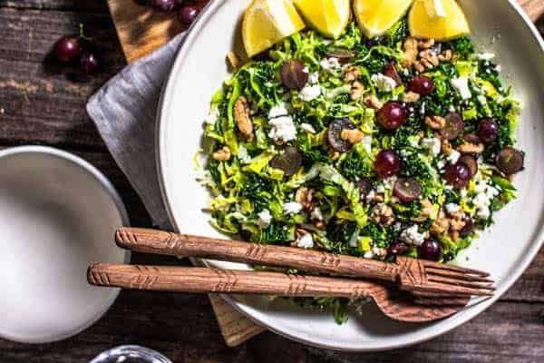 A close up of a Kale Salad recipe with feta, dill, walnuts, and red grapes