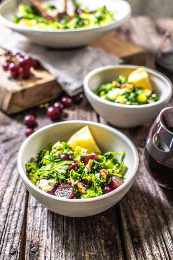 Kale Salad with Red Grapes, Walnuts, and Feta in 2 bowls with glasses of red wine ready to serve