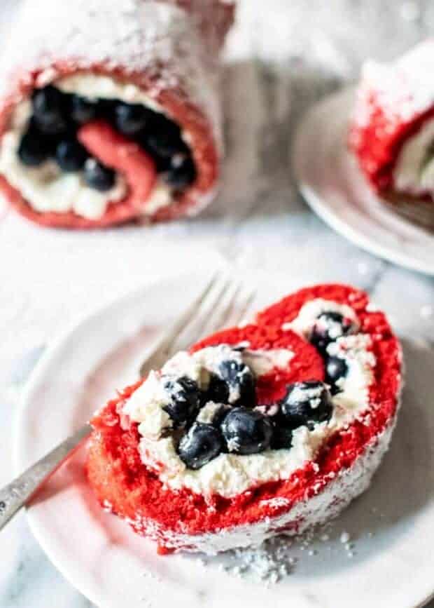 A roll cake that is red filled woth whipped cream and blue berries. 
