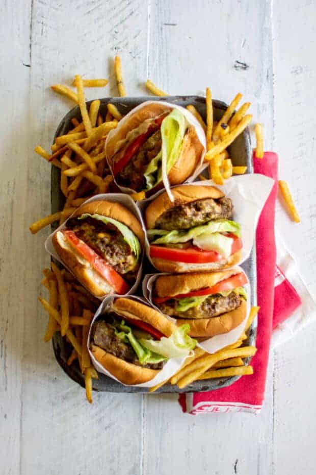 Five juicy burgers on a serving tray with french fries.