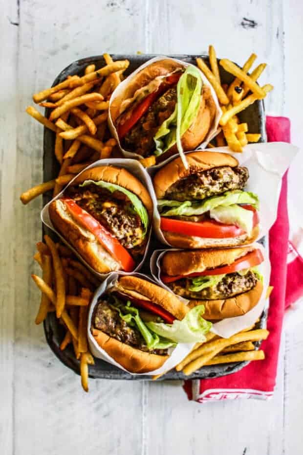 Five burgers with lettuce, tomato, and caramelized onions.