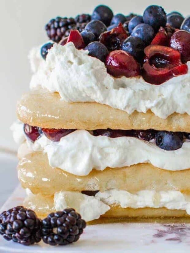 This red, white, and blue dessert cake from the side view. Stacked citrus-caramel soaked Lady Fingers, layered with with mascarpone whipped cream and fresh cherries, blackberries and blueberries
