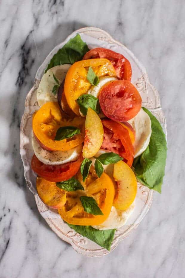 A plate of Caprese Salad with Peaches and yellow and red Heirloom Tomatoes.