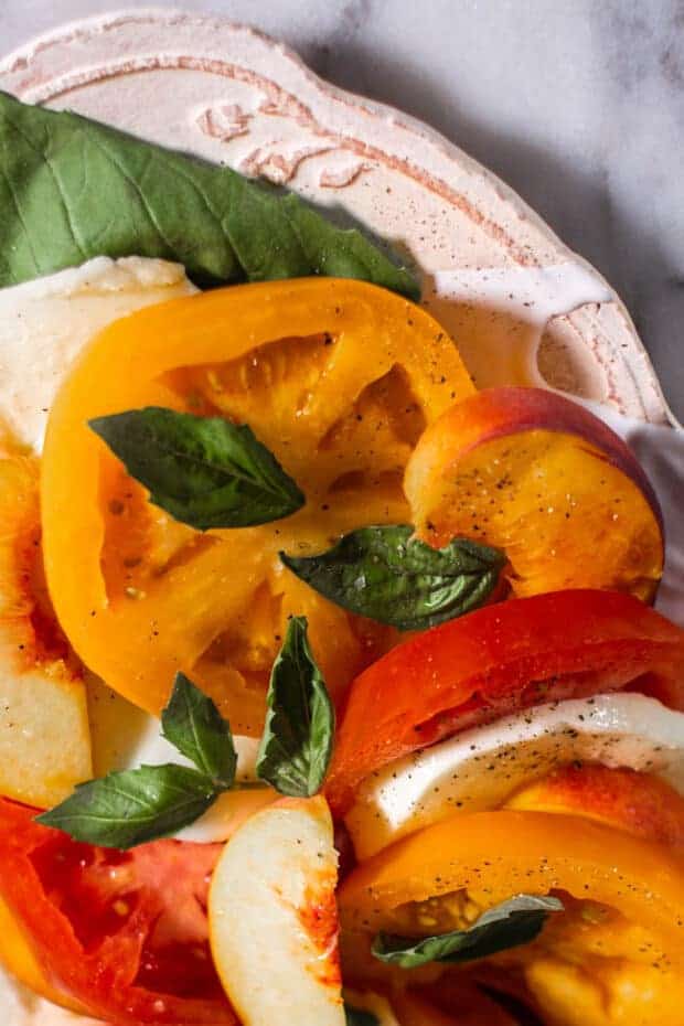 A plate of Caprese Salad with Peaches and yellow and red Heirloom Tomatoes. close up.