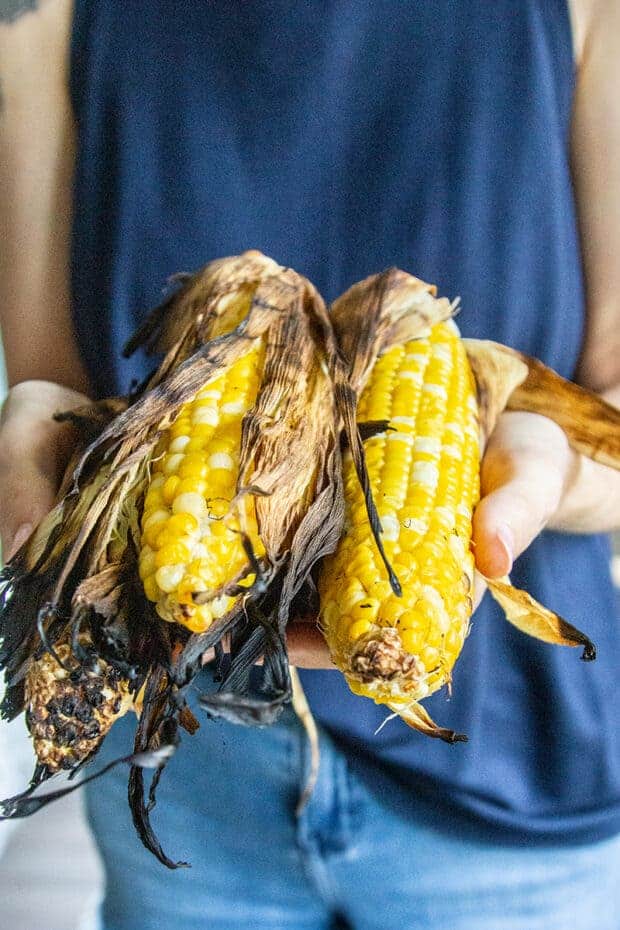 Corn that was grilled in teh husk being held up for the camera.