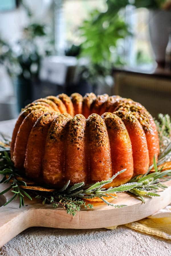 The Easiest Orange Juice Cake on a wooden cake plate with fresh herbs around the base.