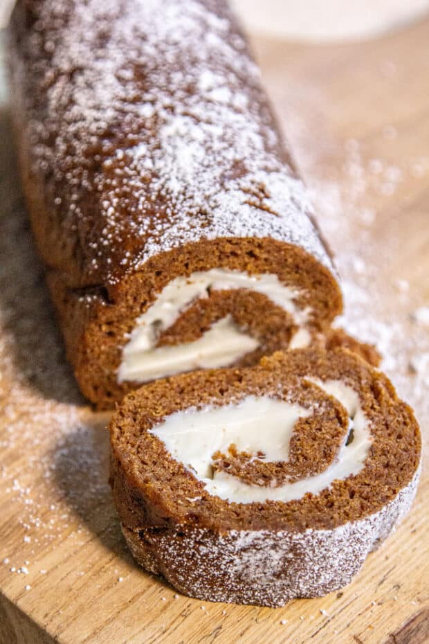 A pumpkin cake roll with one slice removed to show the inside.