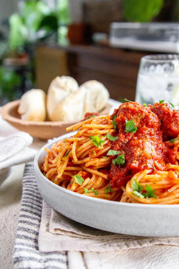 A bowl of pasta next to a basket of bread at the table. 