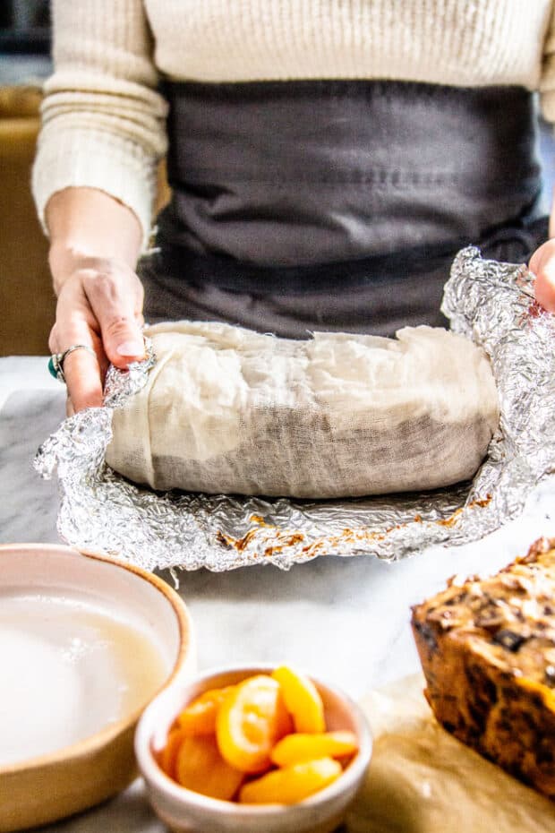 A woman wrapping fruitcake in cheesecloth and foil for aging.