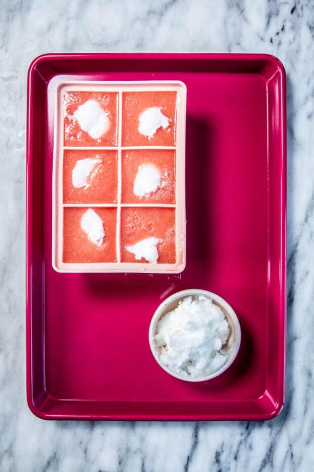 watermelon dog treats in a pink ice cube mold on top of a pink sheet pan.