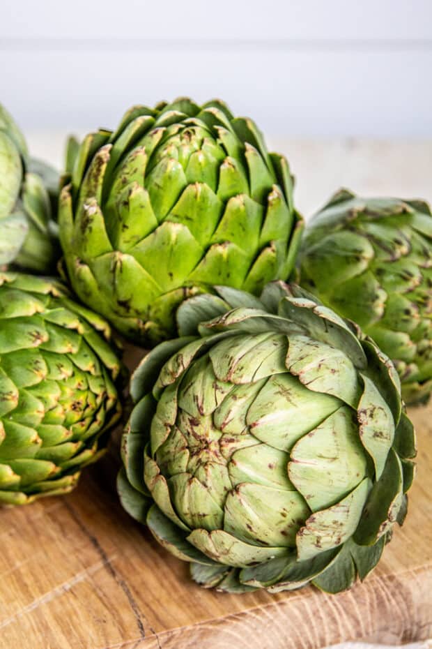 Fresh green globe artichokes on a wooden table.