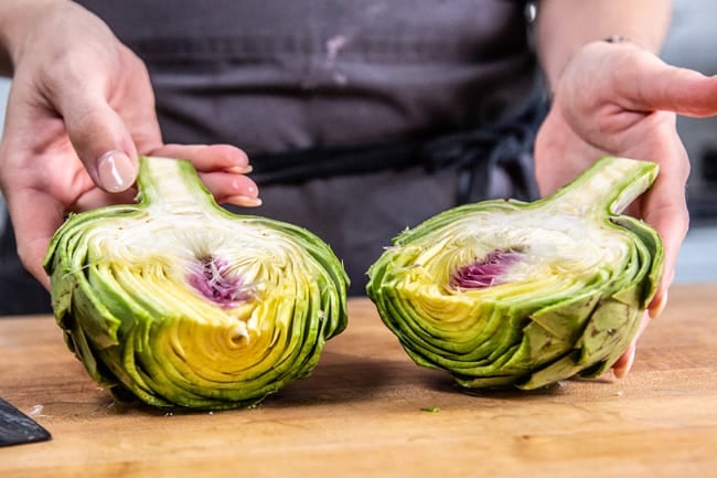 Two halves of one raw artichoke with the entire choke still in place.