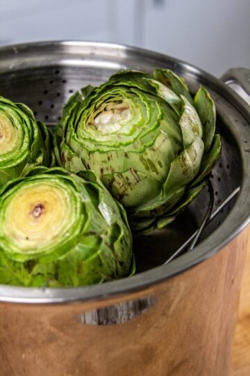 Three whole artichokes with the tops cut off all placed in a steaming rack inside of a large pot