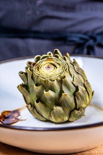 A whole steamed steamed artichoke in a white bowl.