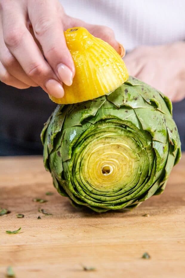 A fully prepped artichoke with the chef rubbing half of a lemon all over it.