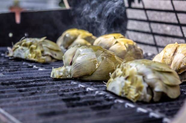 Multiple artichokes face down on a grill with smoke in the air