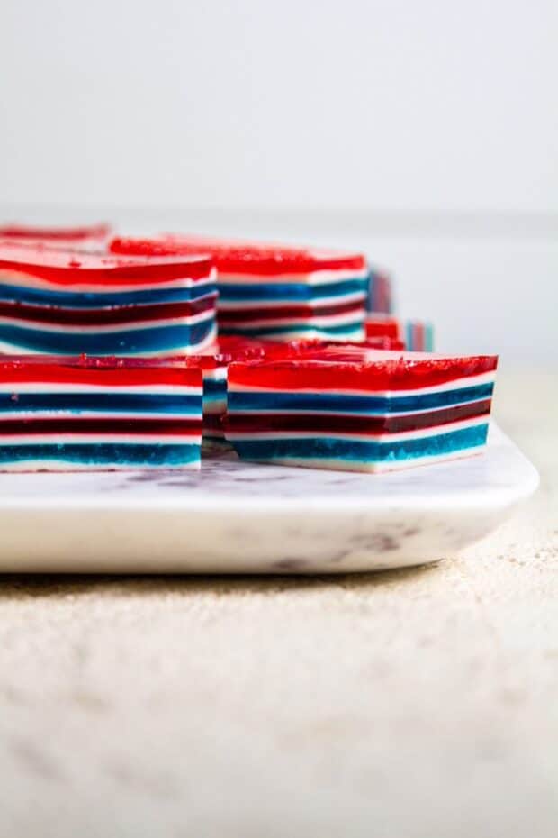 Multiple red, white, and blue stripped jello cake cubes all stacked on a marble slab.