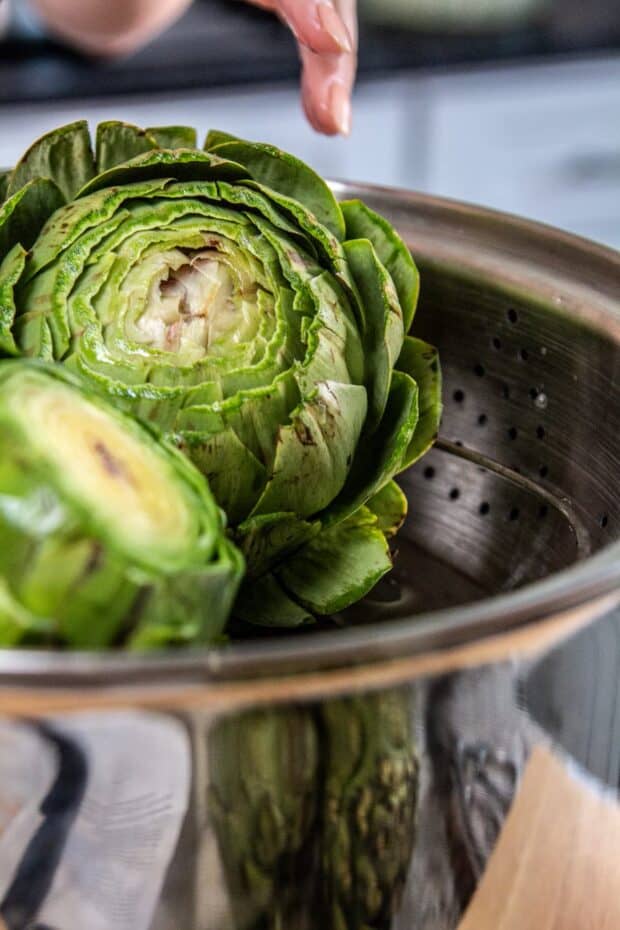 Two whole artichokes with the tops cute off placed stem down into a steamer tray in a big pot