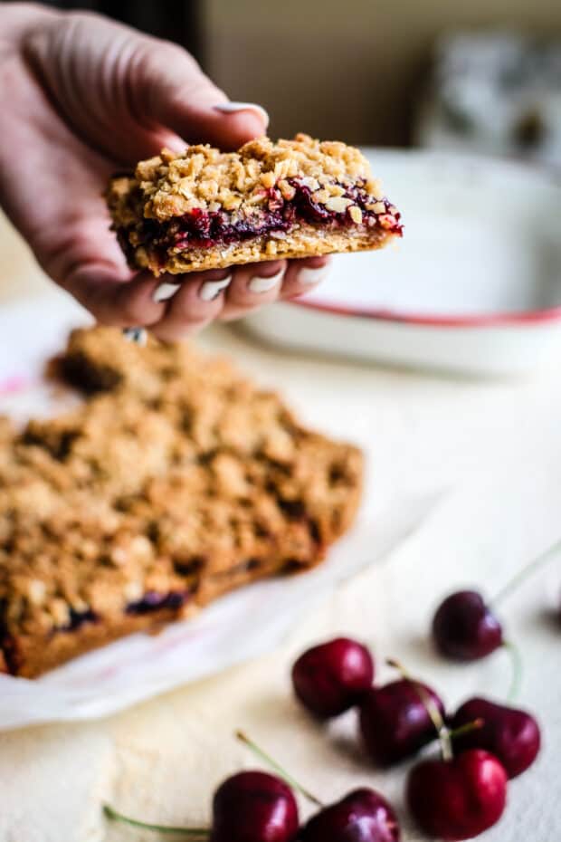 hand holding a cherry oat bar over a batch of oat bars
