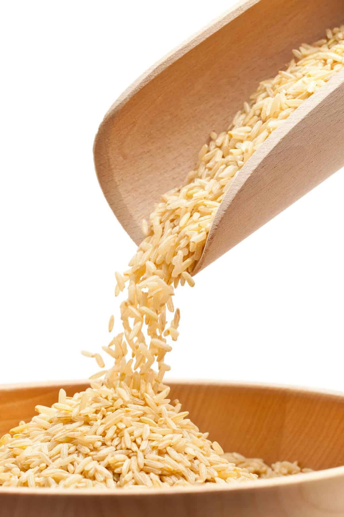 A wooden scoop pouring brown rice into a wooden bowl