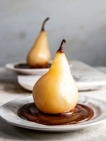 two pears on a plate with hot fudge on a white background