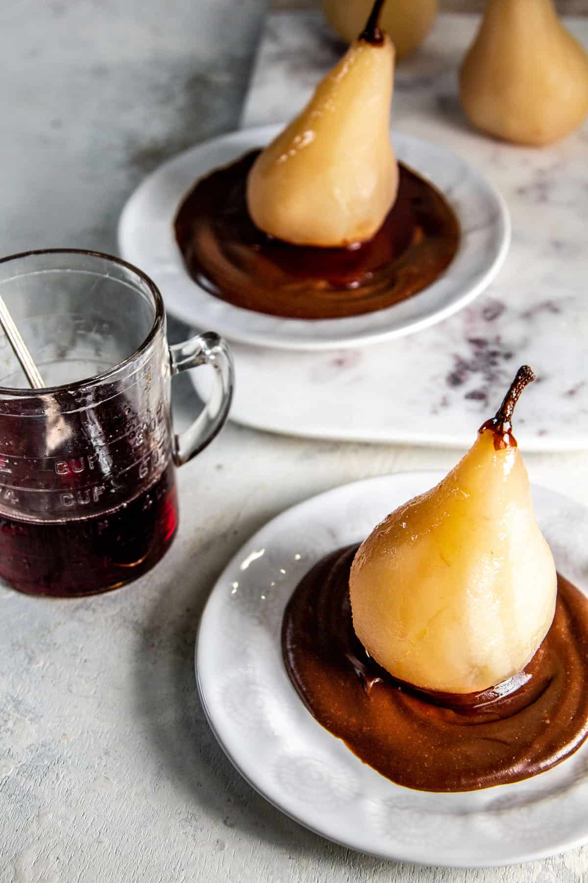 two poached pears on white plates with a bed of hot fudge