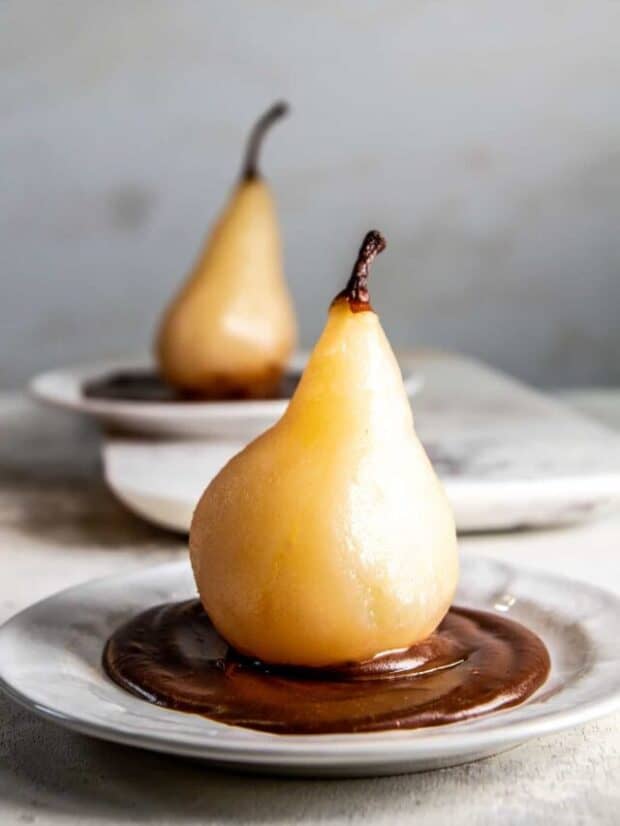 two pears on a plate with hot fudge on a white background