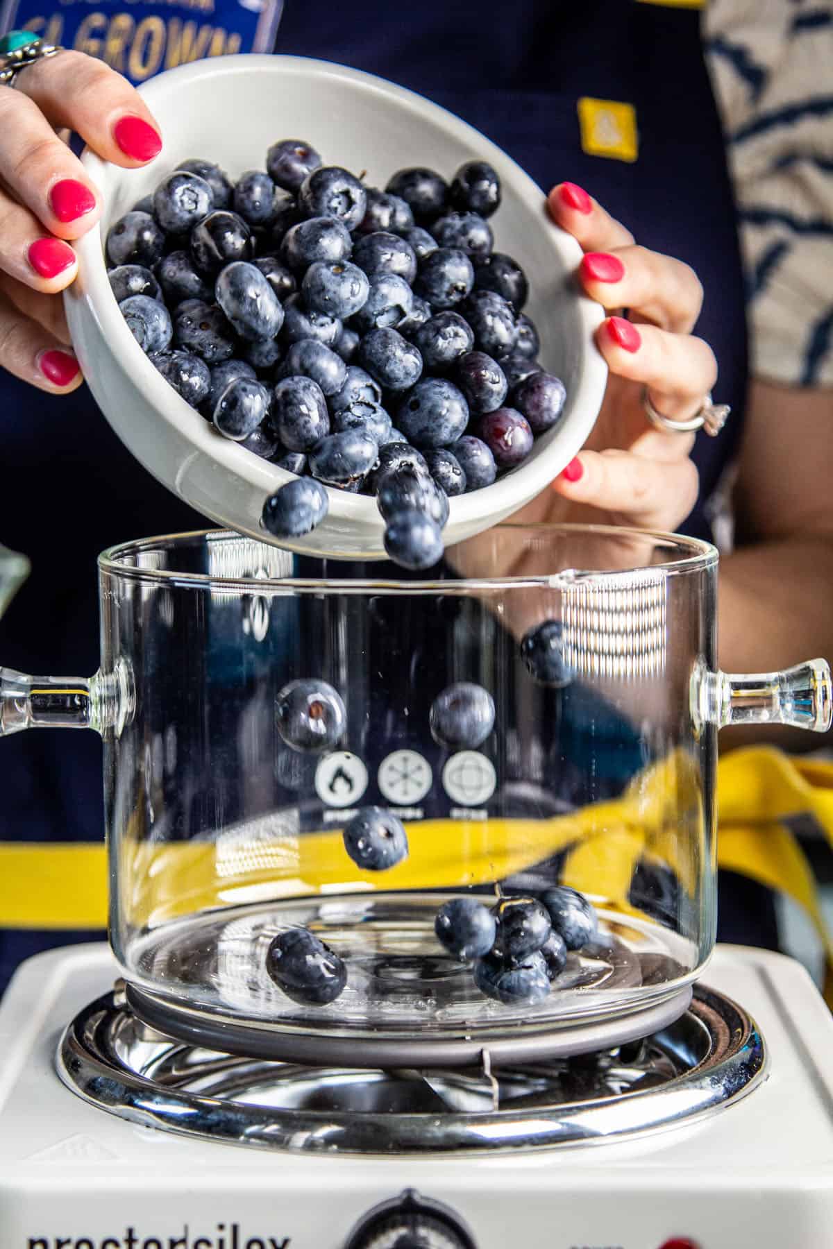Blueberries being poured into a glass saucepan for cooking.