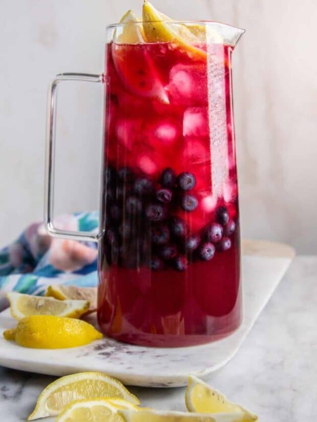 Blueberry lemonade in a glass pitcher ready to serve with fresh blueberries, lemon wedges, adn ice.