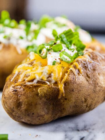 two baked potatoes on a marble board