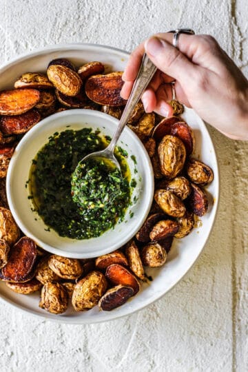 hand holding a spoonful of chimichurri above a bowl of it surrounded by potatoes