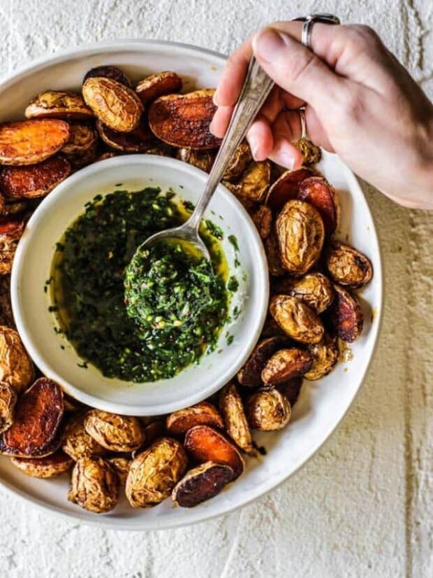 hand holding a spoonful of chimichurri above a bowl of it surrounded by potatoes