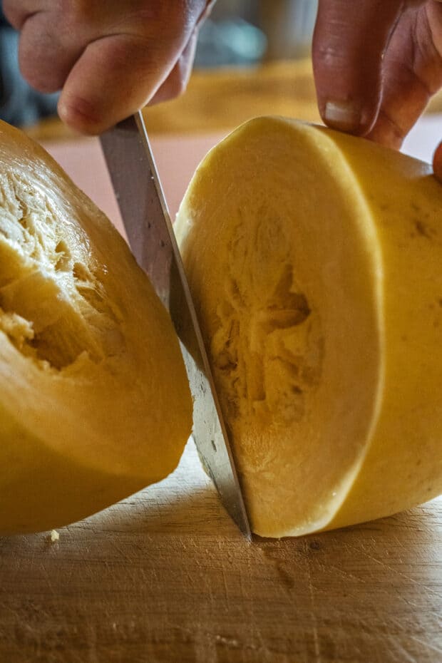 front view of two hands slicing a raw spaghetti squash in half horizontally