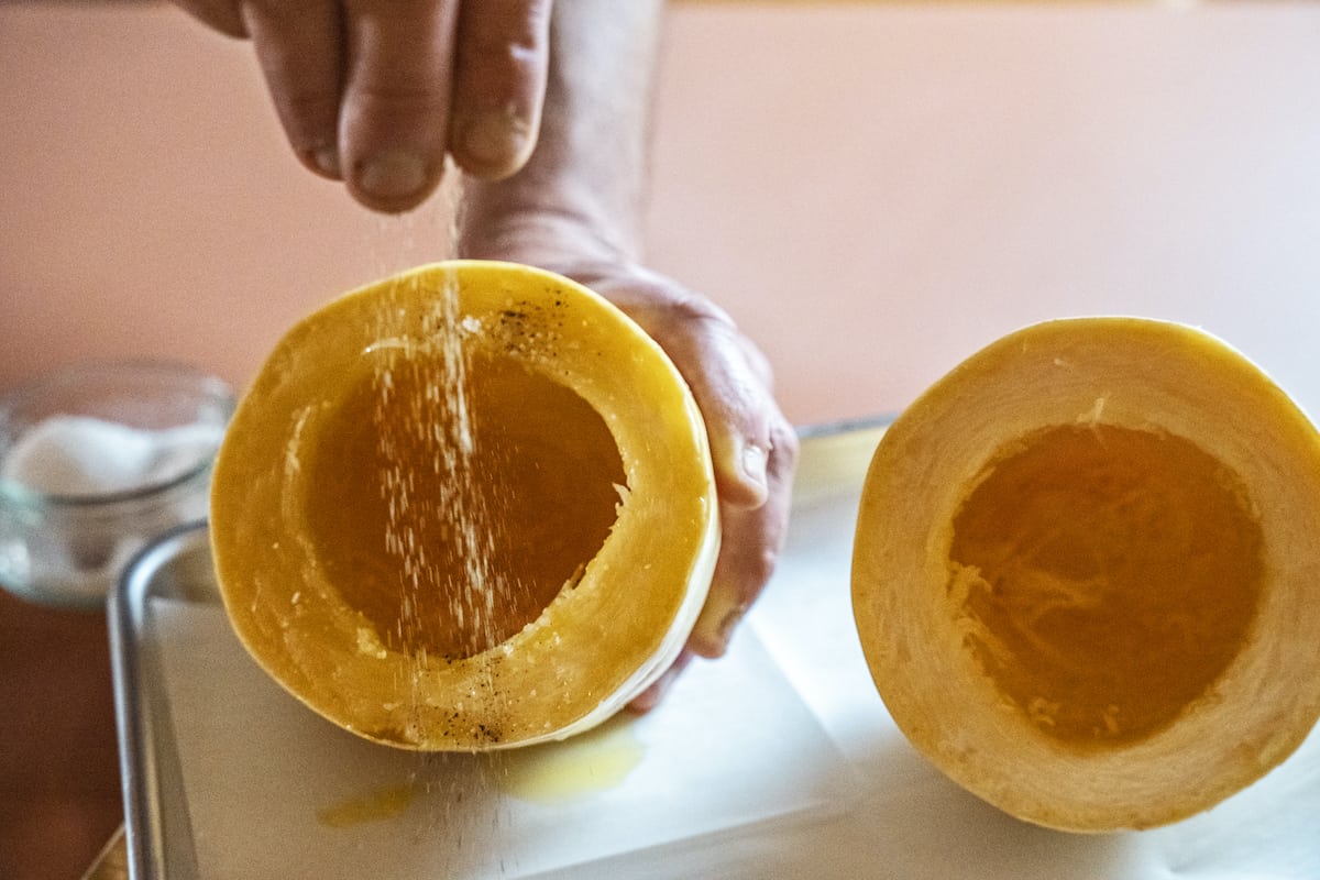 a hand seasoning the flesh of an oiled raw spaghetti squash half with salt