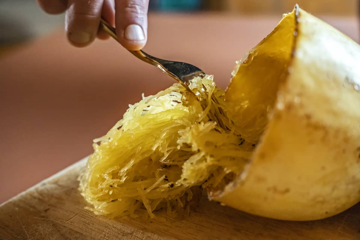 a fork being used to gently pull cooked strands of spaghetti squash from its gourd