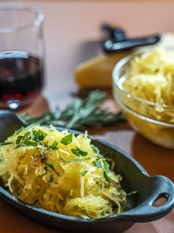 prepared spaghetti squash in a cast iron side dish garnished with chopped parsley. a glass of red is in the background
