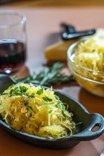 prepared spaghetti squash in a cast iron side dish garnished with chopped parsley. a glass of red is in the background