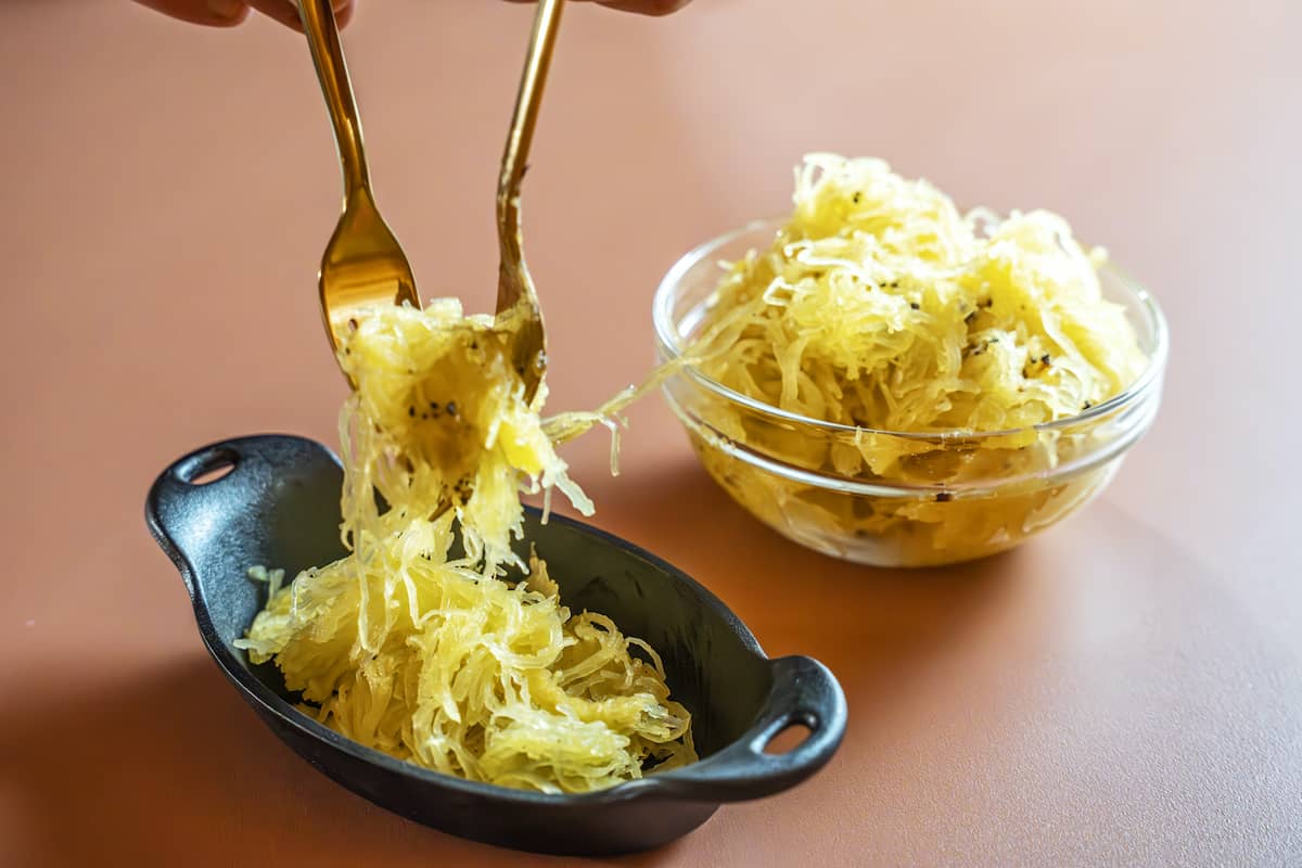 using two forks to plate prepared spaghetti squash strands from a bowl to a cast iron side dish