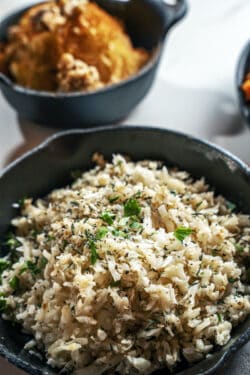 close shot of cooked cauliflower rice, garnished with herbs in a cast iron skillet