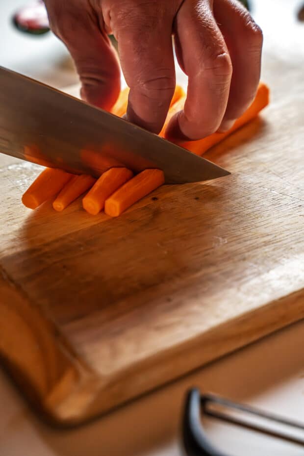 hands cutting carrots on a wooden cutting board