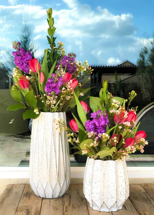 two vases full of flowers in front of a window