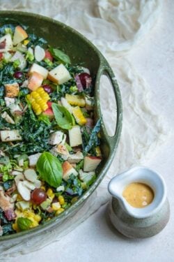 A big salad next to a small pitcher of dressing made with mostarda.